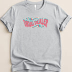 Gray t-shirt with "DRUG DEALER" text in a wavy, pastel pink and blue font.