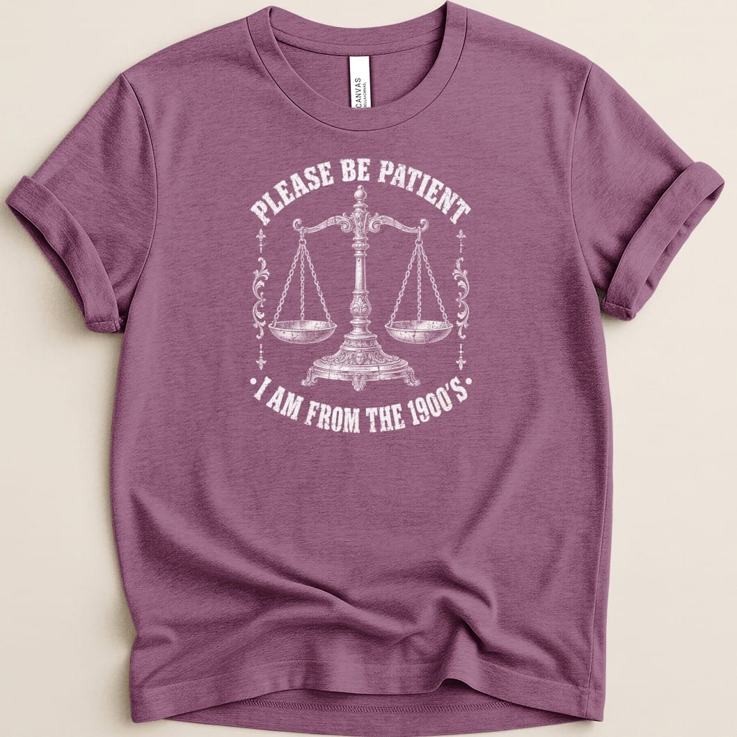 Purple t-shirt with white text and scales graphic: "PLEASE BE PATIENT · I AM FROM THE 1900'S."