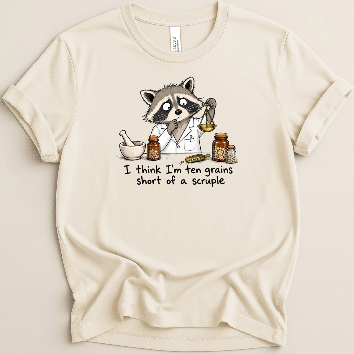 Cream t-shirt with cartoon raccoon in lab coat, weighing scale, mortar and pestle, and text.