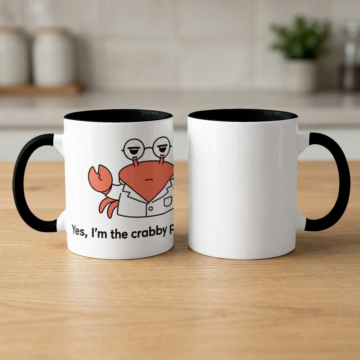 Two white mugs with black rims and handles, one with a crab graphic and text.