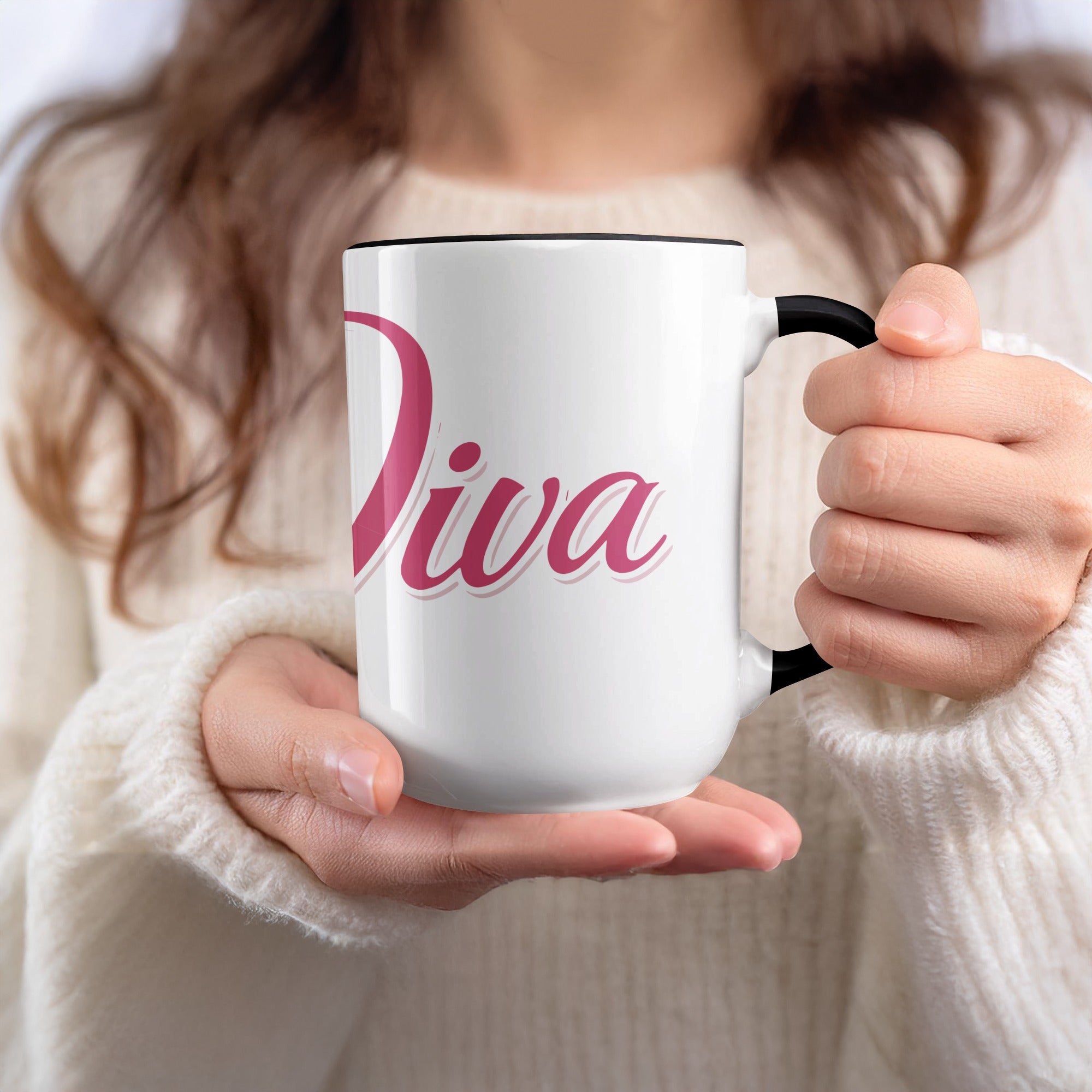White mug with pink text "Diva" held by a person.
