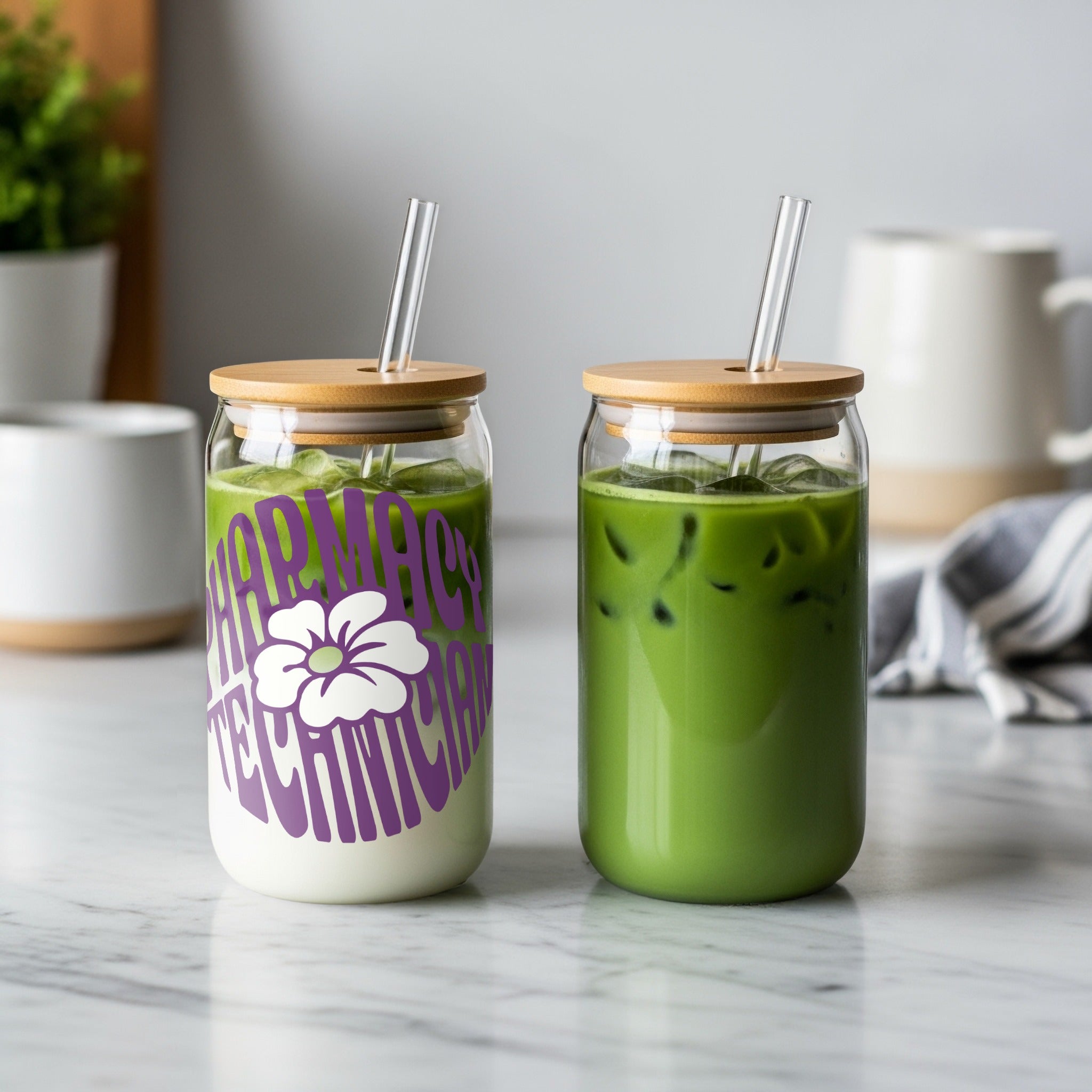 Two glass cups with lids and straws, one with matcha, one with a purple floral design.