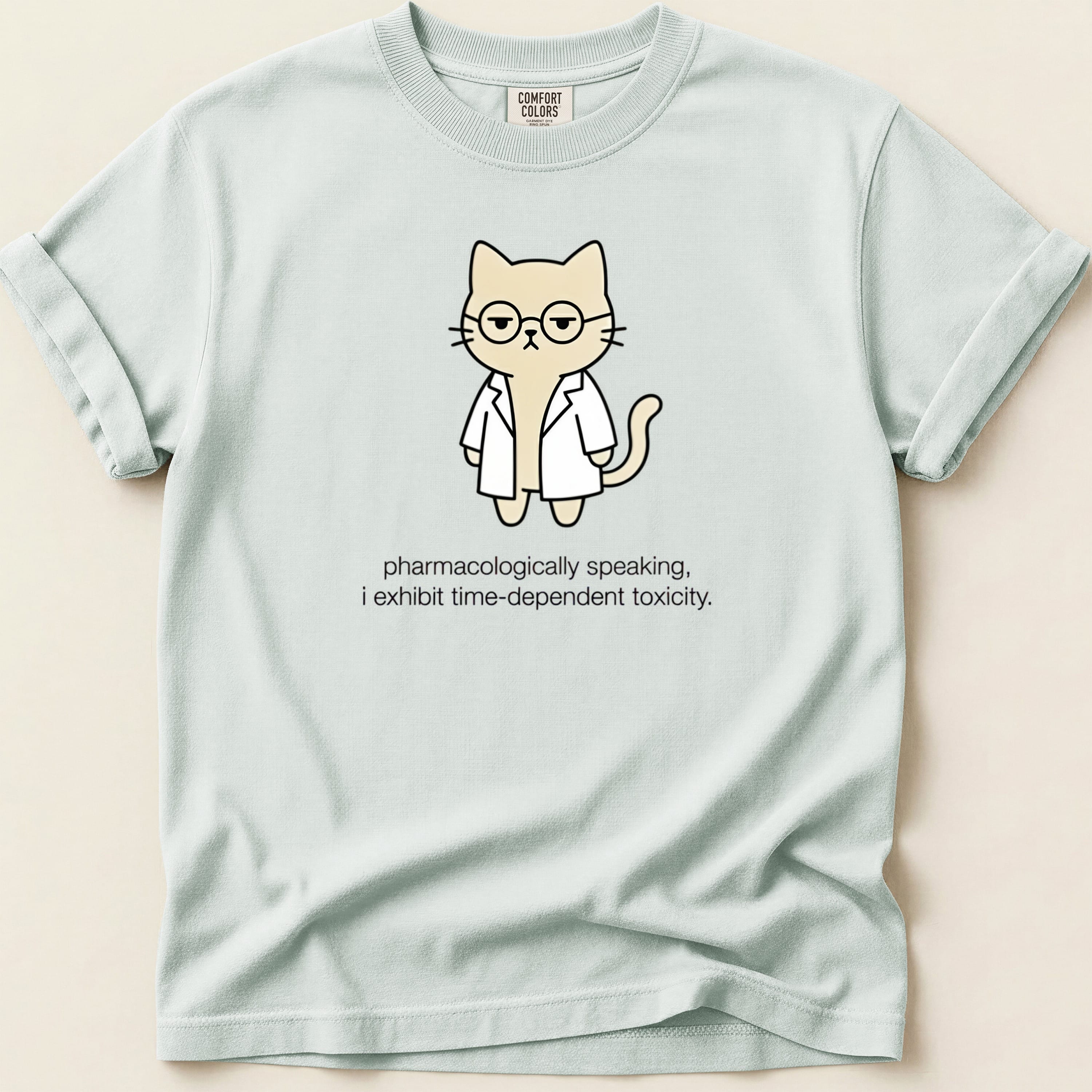 Light blue t-shirt with a cartoon cat in a lab coat wearing glasses, text reads "pharmacologically speaking, i exhibit time-dependent toxicity."