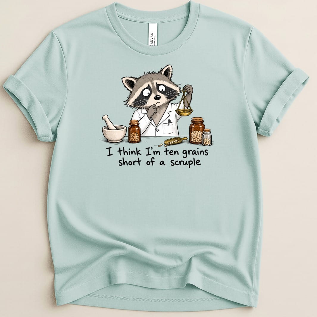 T-shirt graphic with raccoon in lab coat, weighing scale, mortar, and jars, text: I think I'm ten grains short of a scruple.