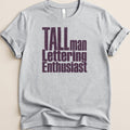 Light grey t-shirt with "TALLman Lettering Enthusiast" text in distressed purple.