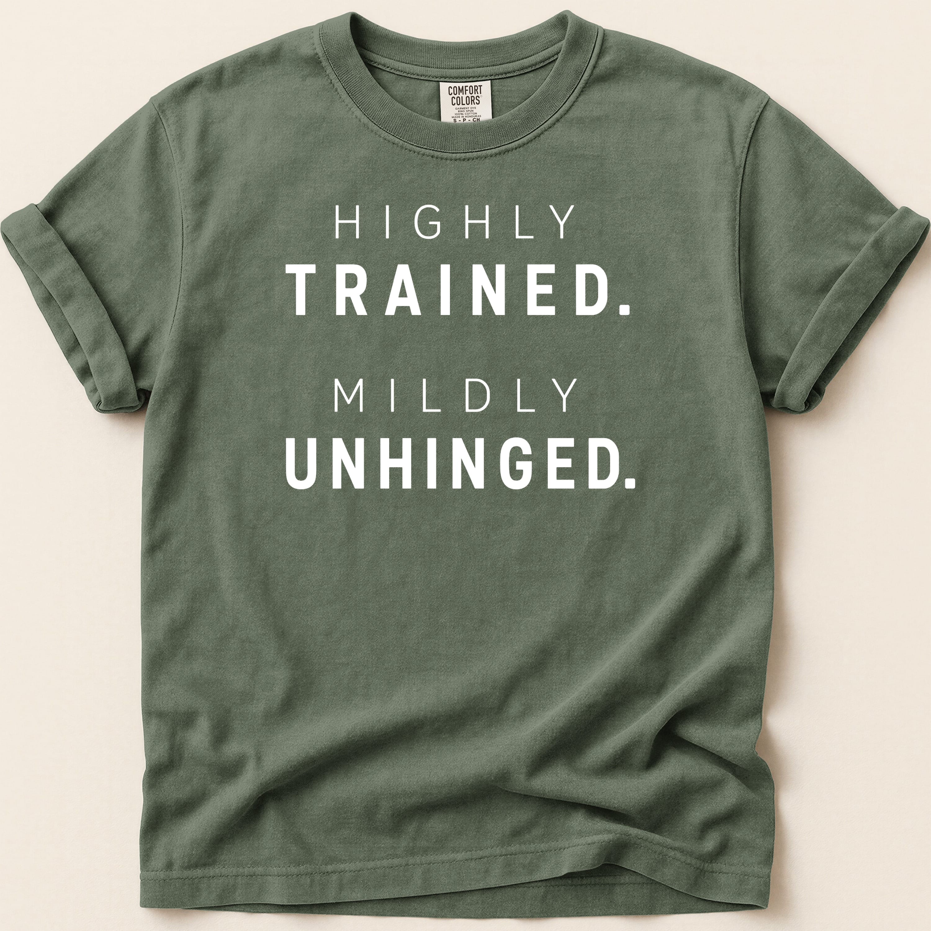 Green t-shirt with "HIGHLY TRAINED. MILDLY UNHINGED." text.