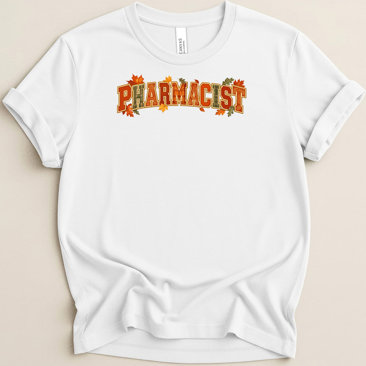 A white short-sleeved t-shirt with rolled cuffs features the word PHARMACIST in fall colors and autumn leaves.