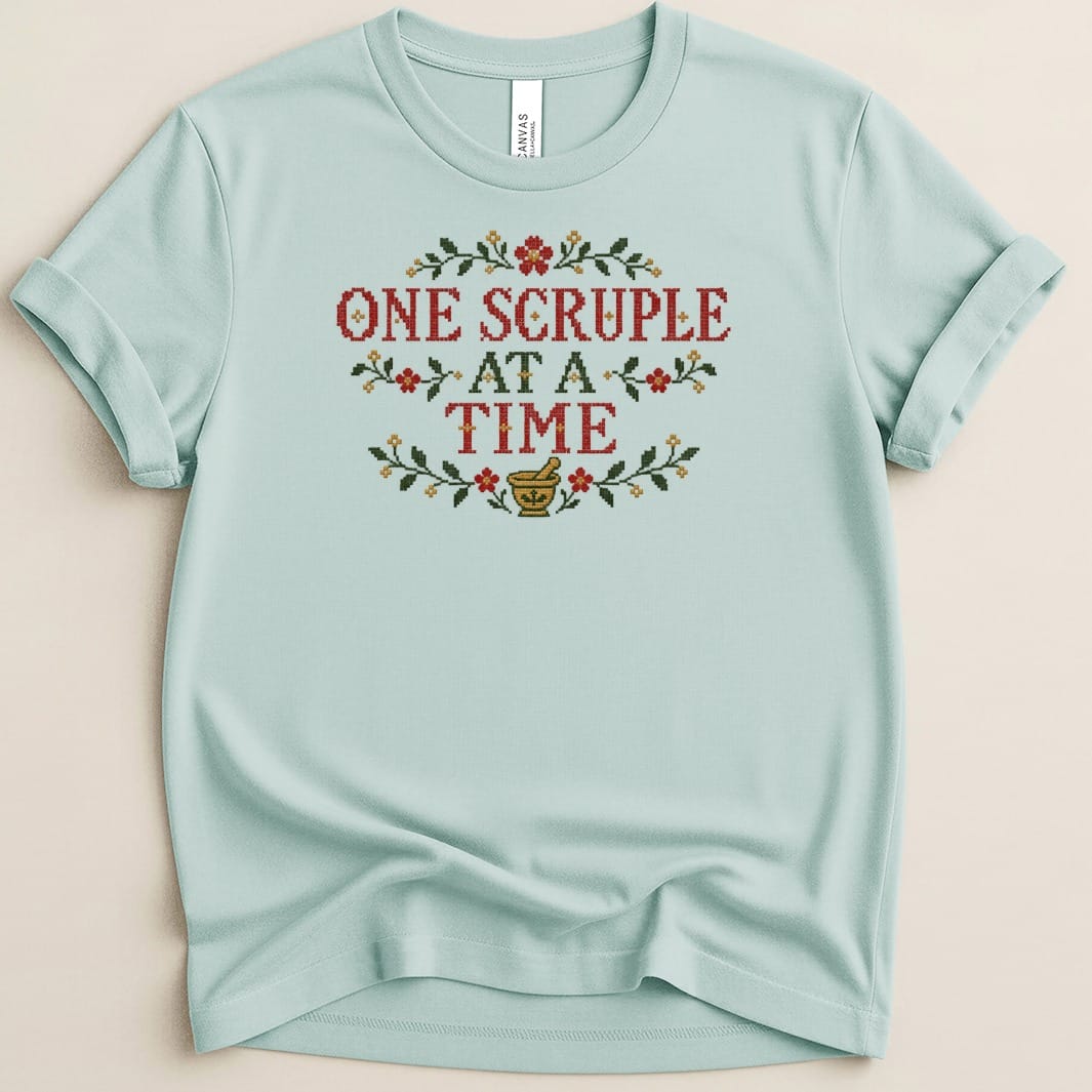 Light blue t-shirt featuring cross-stitch embroidery with the text "One Scruple at a Time" and floral motifs.
