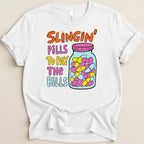 White t-shirt with "Slingin' Pills To Pay The Bills" text and a jar of pills.