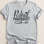 Grey t-shirt with "Retired Pharmacist" text and a capsule graphic.
