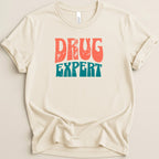 Cream t-shirt with distressed "DRUG EXPERT" text in orange and teal.