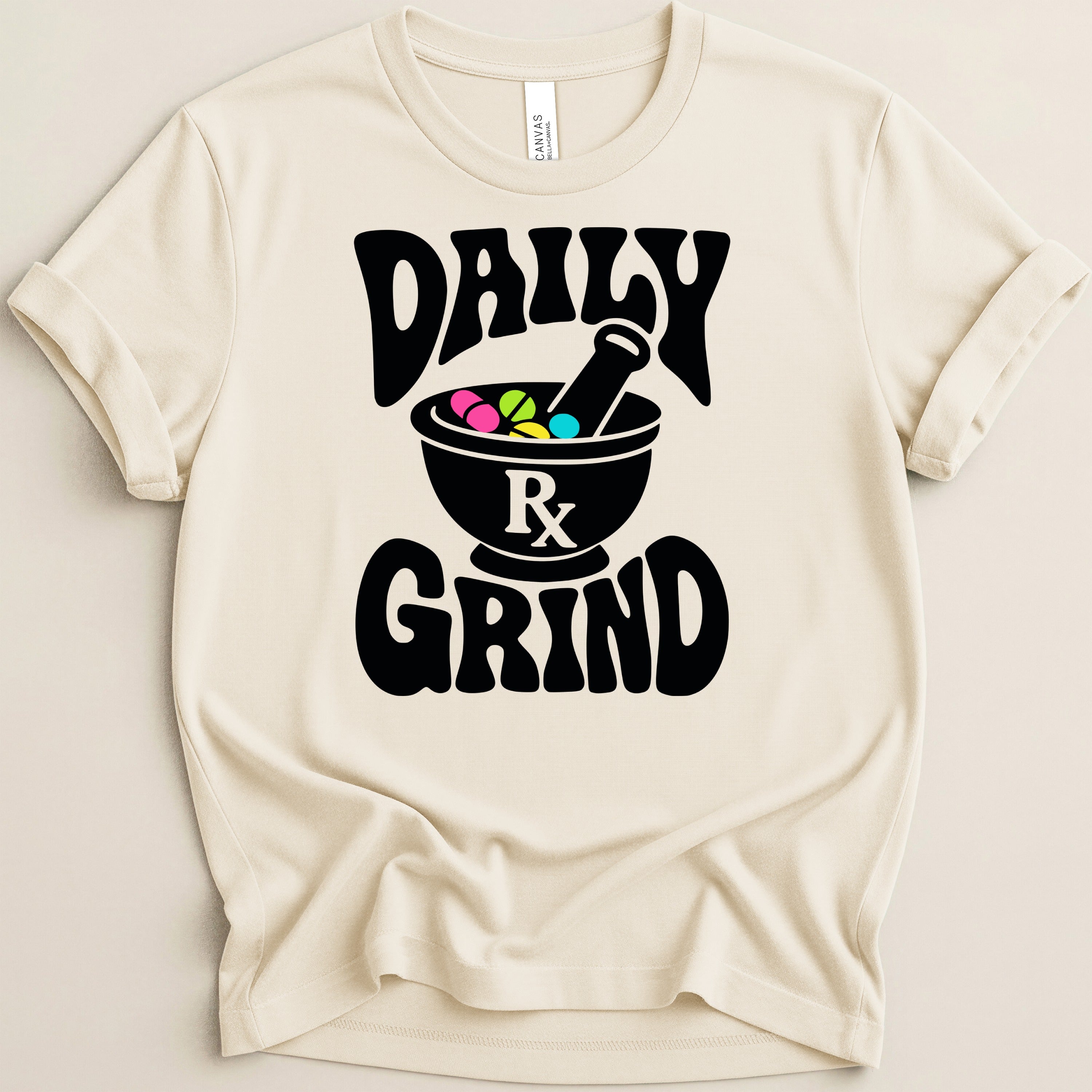 Cream t-shirt with black text "DAILY GRIND" and a mortar and pestle full of colorful pills.