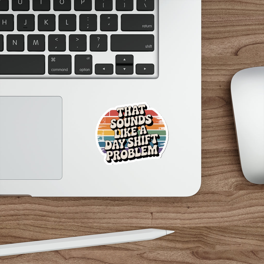 Sticker with text "THAT SOUNDS LIKE A DAY SHIFT PROBLEM" on a laptop.