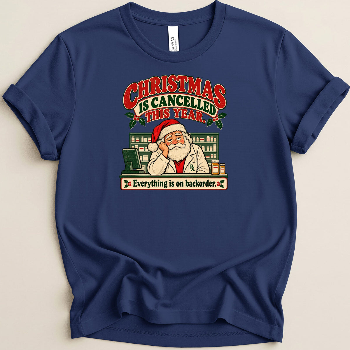 A dark blue t-shirt printed with a graphic of Santa Claus as a pharmacist behind a pharmacy counter with text reading Christmas is cancelled this year.