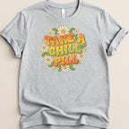 Grey t-shirt with "TAKE A CHILL PILL" in retro font surrounded by daisies.