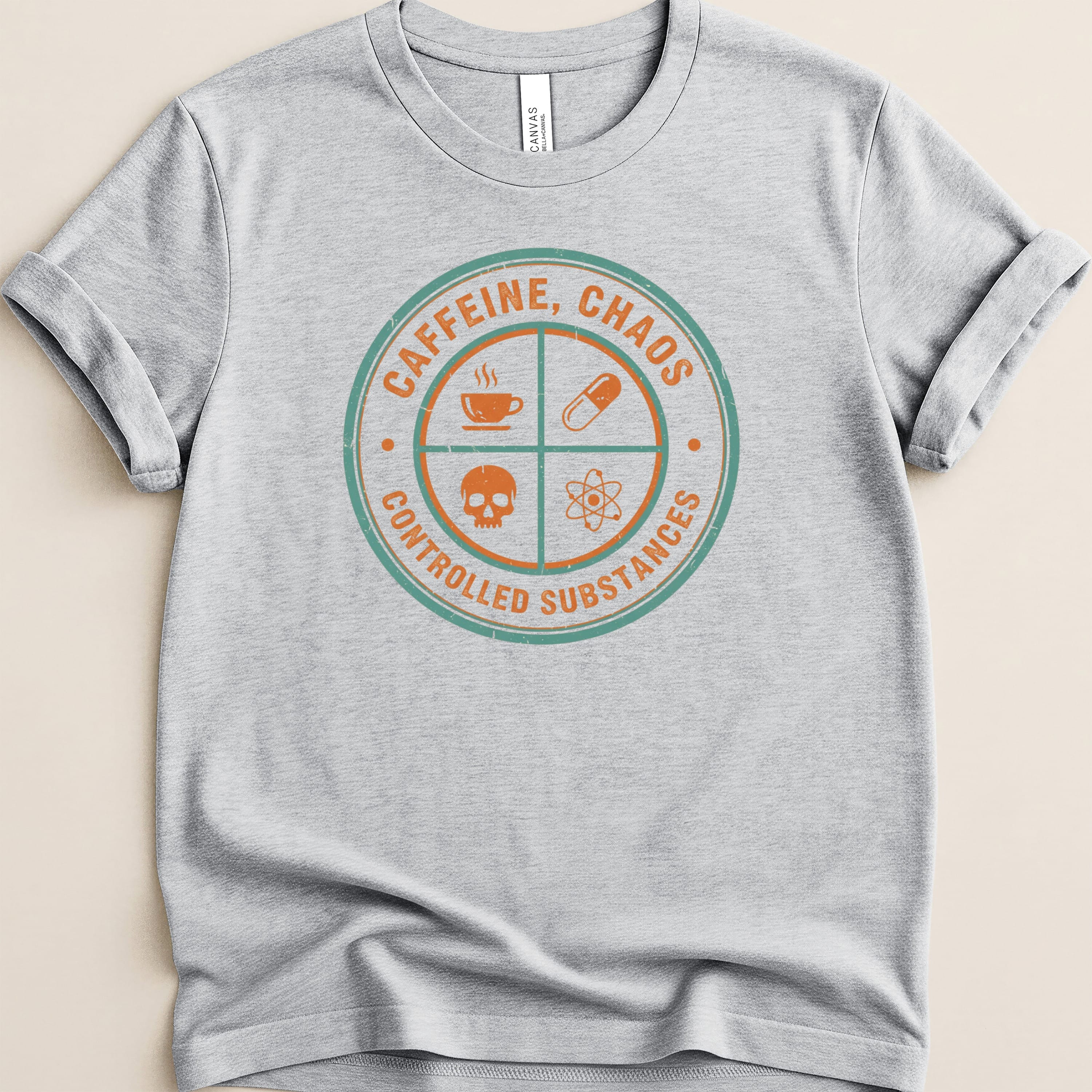 Grey t-shirt with circular graphic reading "CAFFEINE, CHAOS CONTROLLED SUBSTANCES" and icons.