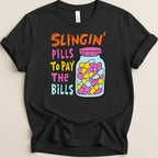 Black t-shirt with "Slingin' Pills To Pay The Bills" text and pill bottle graphic.