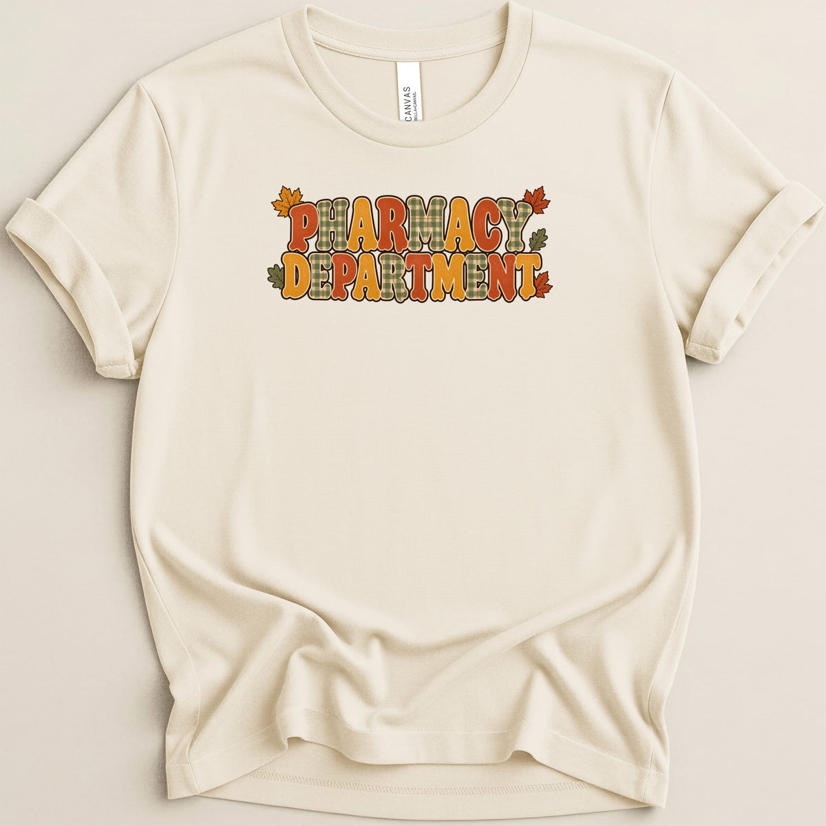 A cream-colored t-shirt with rolled sleeves featuring the text Pharmacy Department in autumn-colored bubble letters.