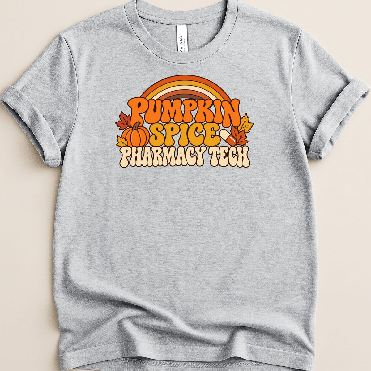 A heather gray t-shirt featuring a retro graphic that reads Pumpkin Spice Pharmacy Tech with a pumpkin, leaves, and capsule.