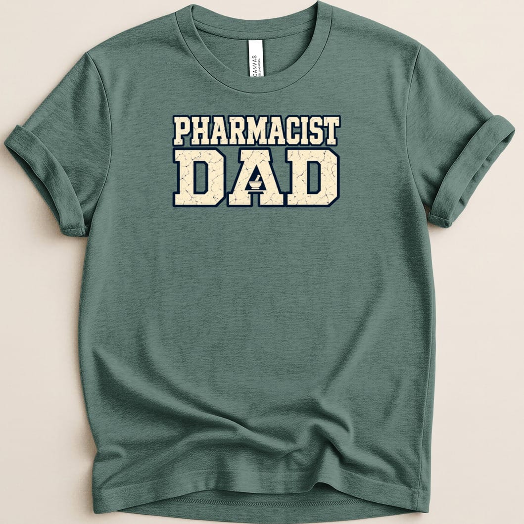 A dark green short-sleeved t-shirt with rolled cuffs and distressed white text reading PHARMACIST DAD centered on the chest.