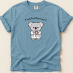 Blue t-shirt with cartoon koala in pharmacist coat holding prescription bottle.