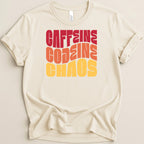 Cream t-shirt with "CAFFEINE CHAOS" text in red, orange, and yellow wavy font.