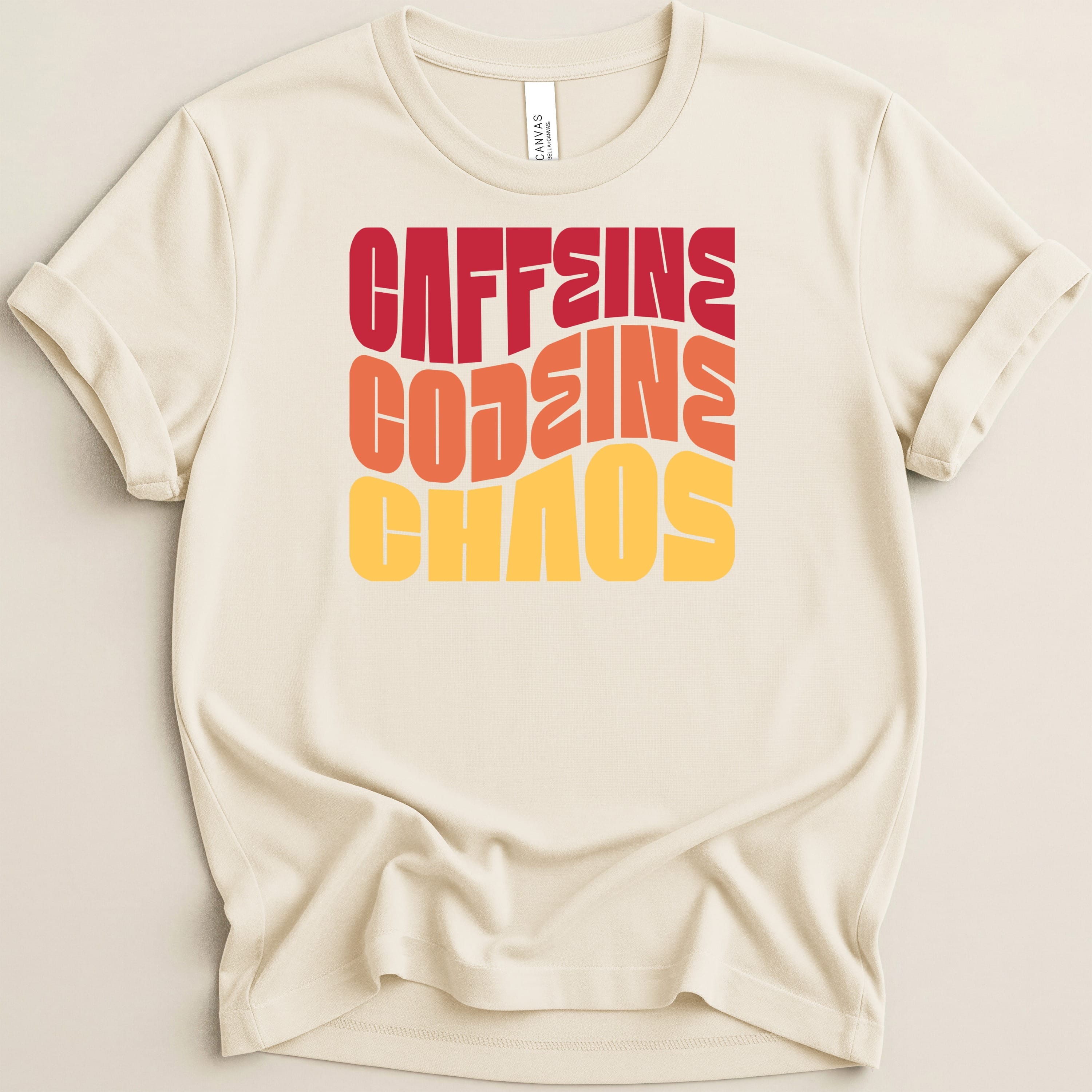 Cream t-shirt with "CAFFEINE CHAOS" text in red, orange, and yellow wavy font.
