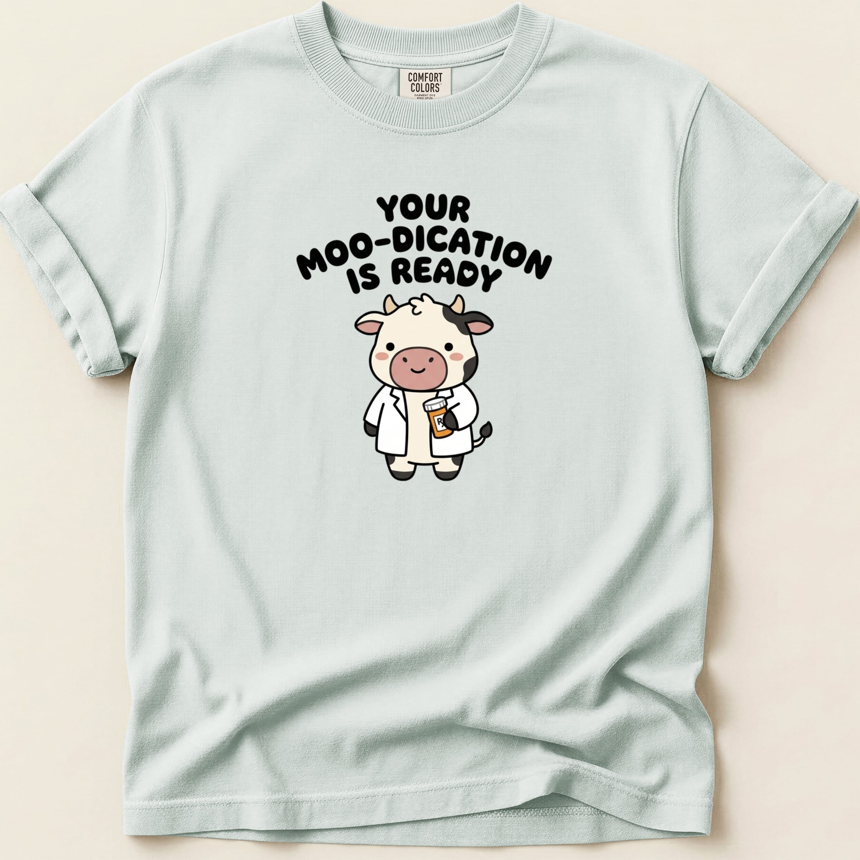 White t-shirt with cartoon cow wearing lab coat and text "Your moo-dication is ready".