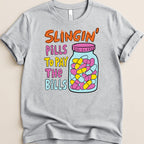 Grey t-shirt with multicolor text and a jar of pills graphic.
