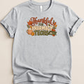 A gray t-shirt featuring the text Thankful For Pharmacy Techs surrounded by autumn leaves, a coffee mug, and a pill counting tray.