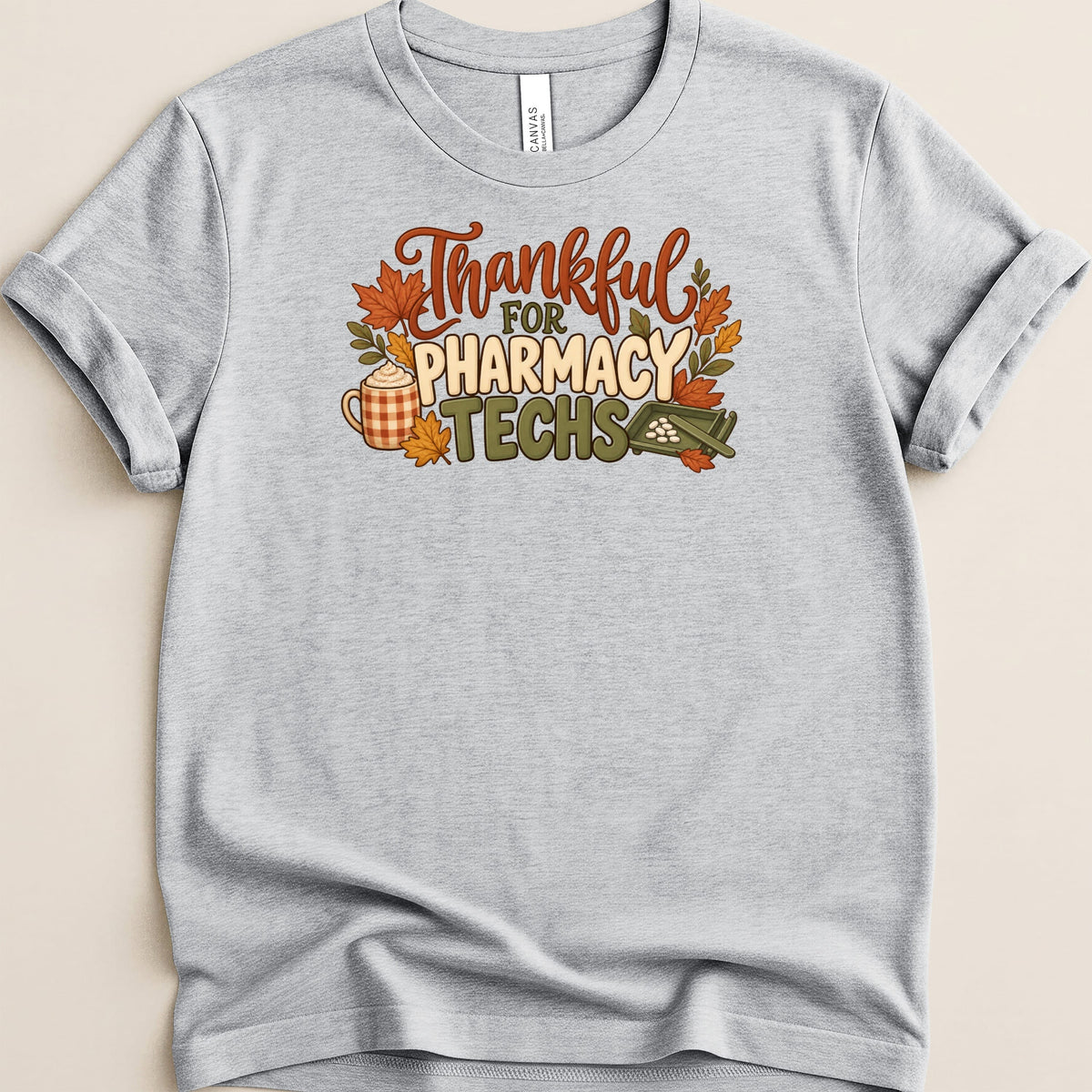 A gray t-shirt featuring the text Thankful For Pharmacy Techs surrounded by autumn leaves, a coffee mug, and a pill counting tray.