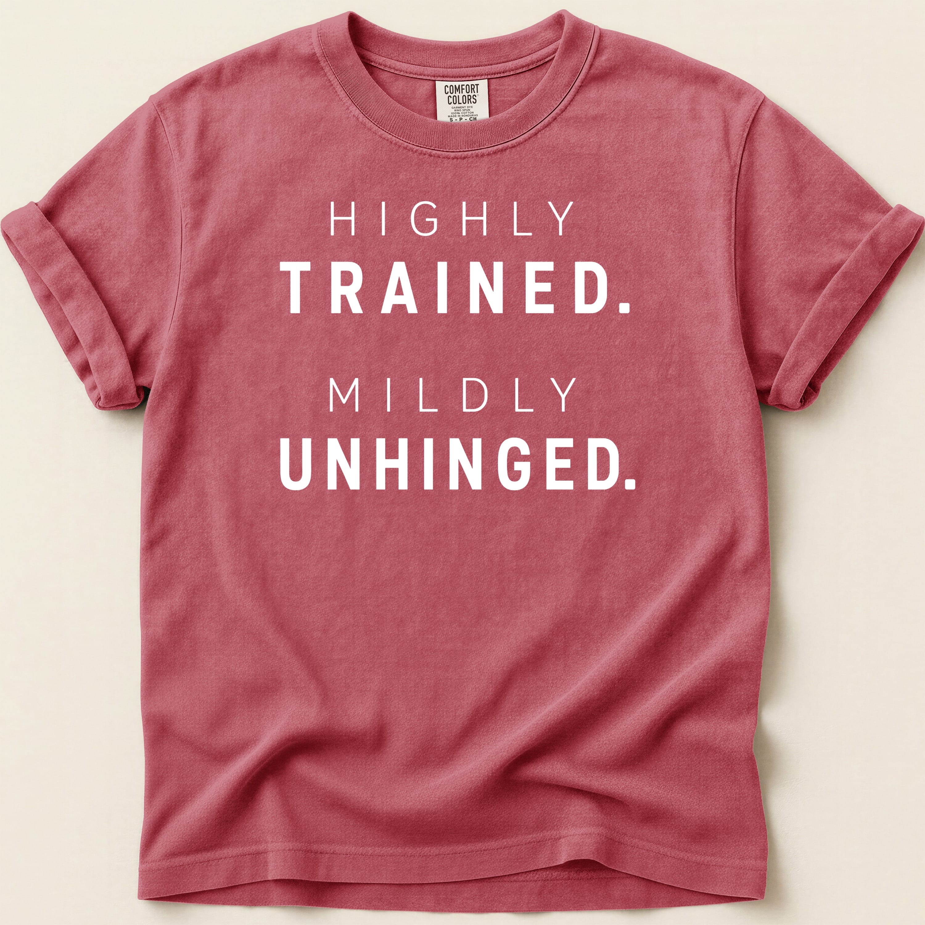 Red t-shirt with "HIGHLY TRAINED. MILDLY UNHINGED." printed in white text.