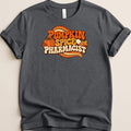 Dark gray t-shirt with retro orange graphic text reading Pumpkin Spice Pharmacist, featuring a pumpkin and pill capsule.