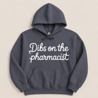 Dark gray hoodie with white cursive text "Dibs on the pharmacist".