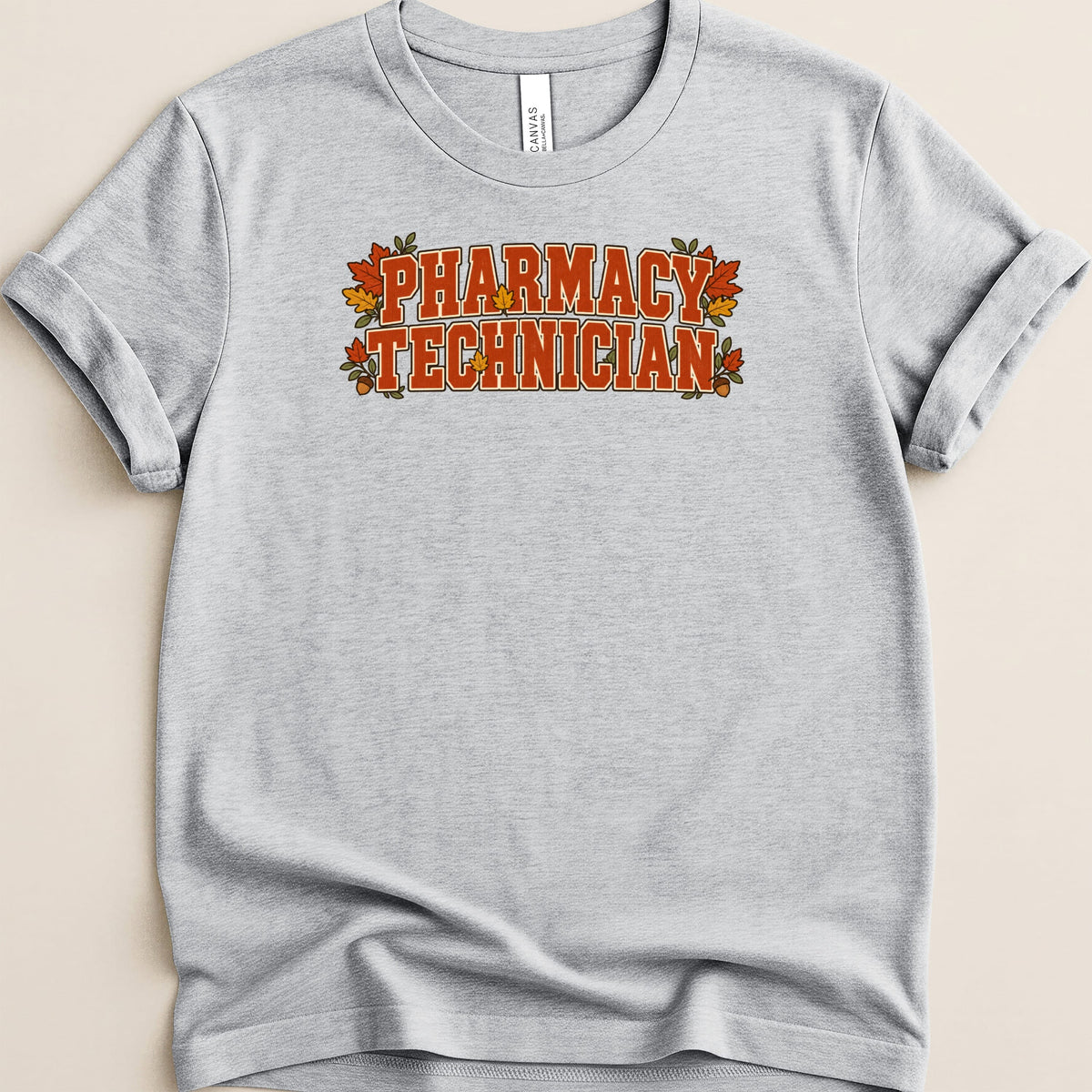 A heather gray t-shirt with rolled sleeves features orange lettering that reads "PHARMACY TECHNICIAN" framed by autumn leaves.