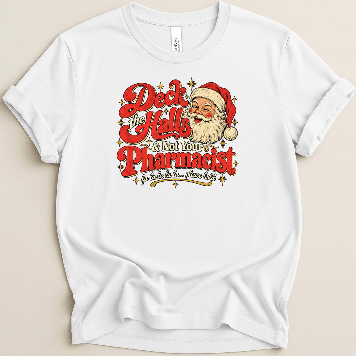 A white short-sleeved t-shirt with a vintage-style graphic featuring Santa Claus and the text "Deck the Halls & Not Your Pharmacist".