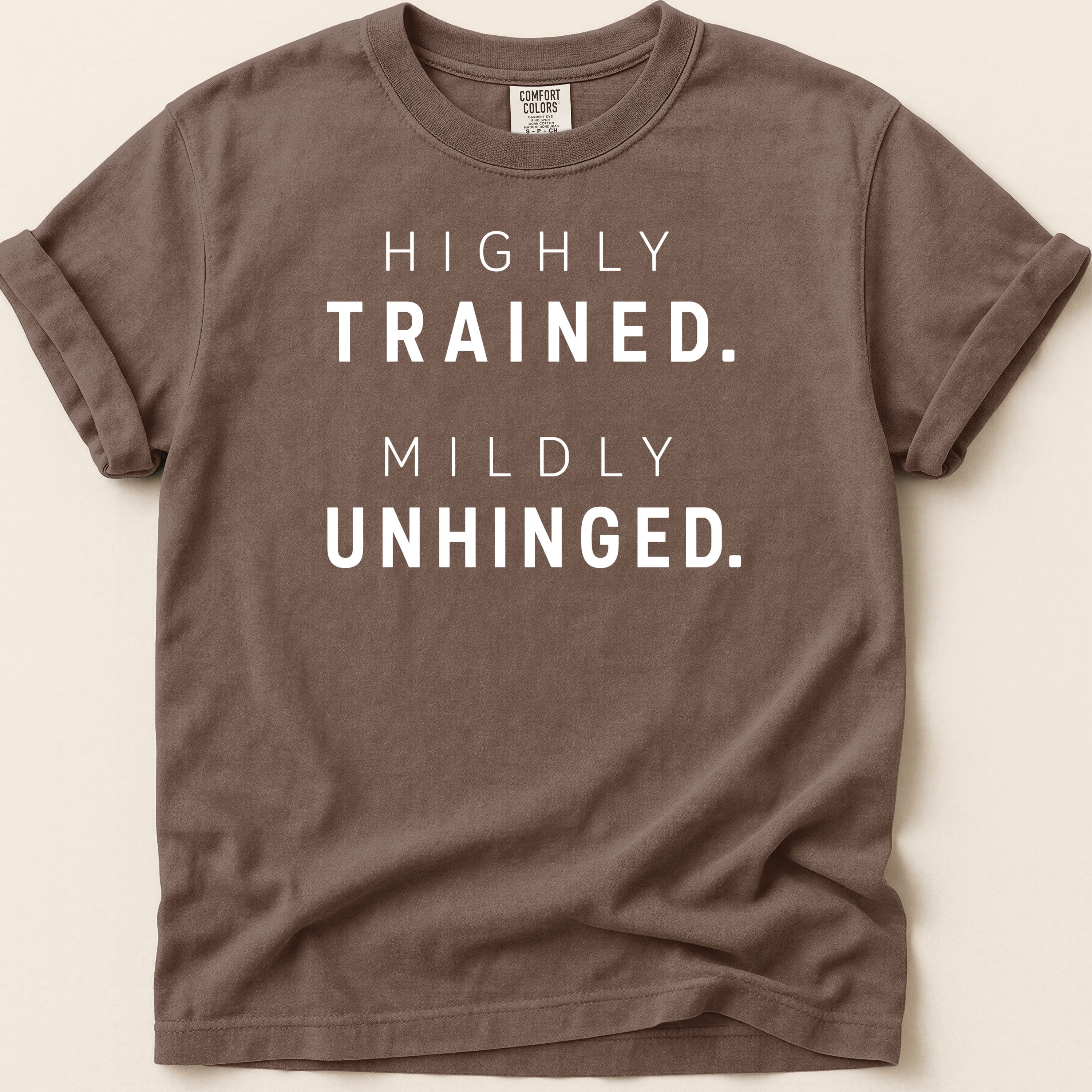 Brown t-shirt with "HIGHLY TRAINED. MILDLY UNHINGED." text.