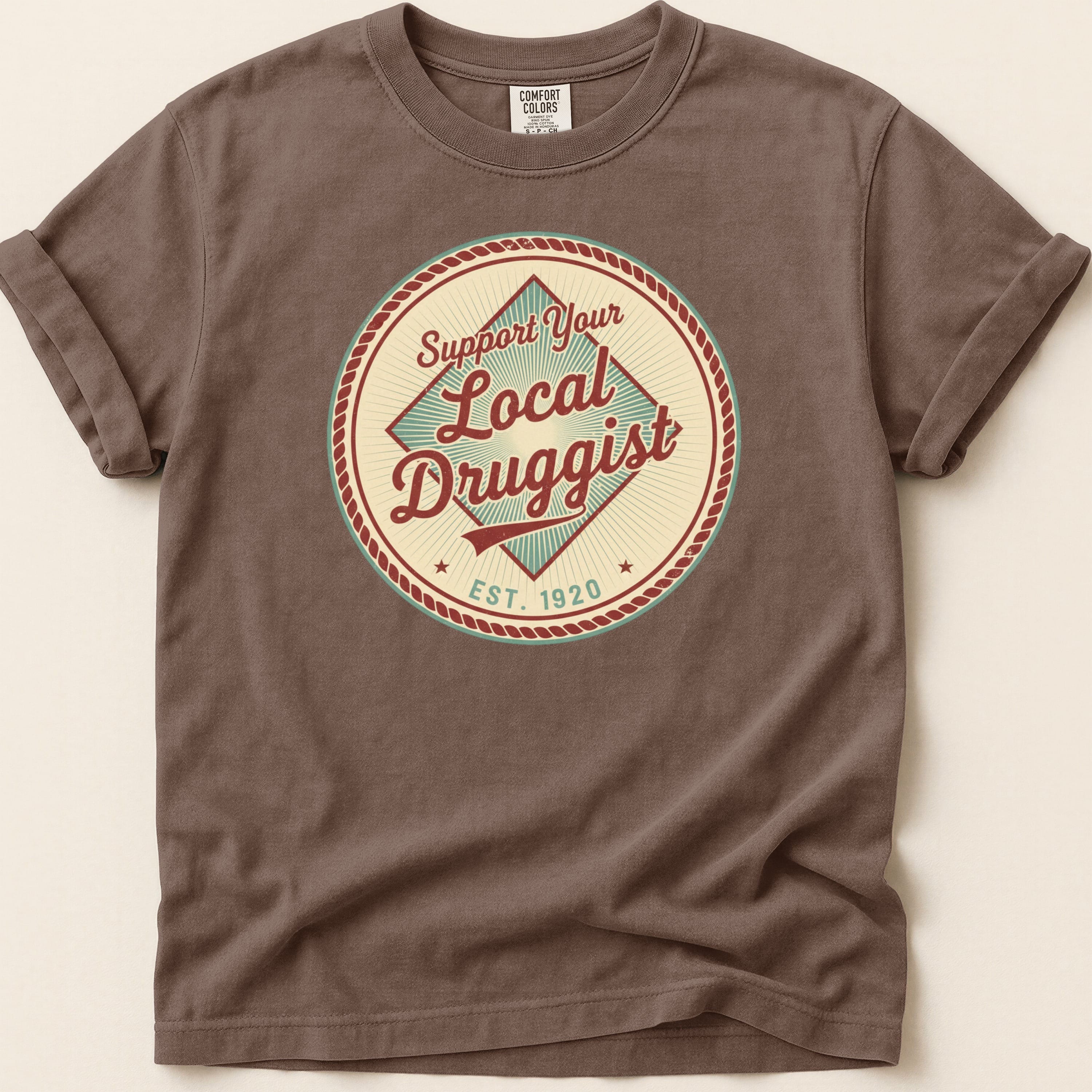 Brown t-shirt with circular "Support Your Local Druggist EST. 1920" graphic.