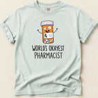 Light blue Comfort Colors shirt with a cartoon pill bottle and "World's Okayest Pharmacist" text.