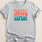 Gray t-shirt with "DRUG EXPERT" in distressed orange and teal text.