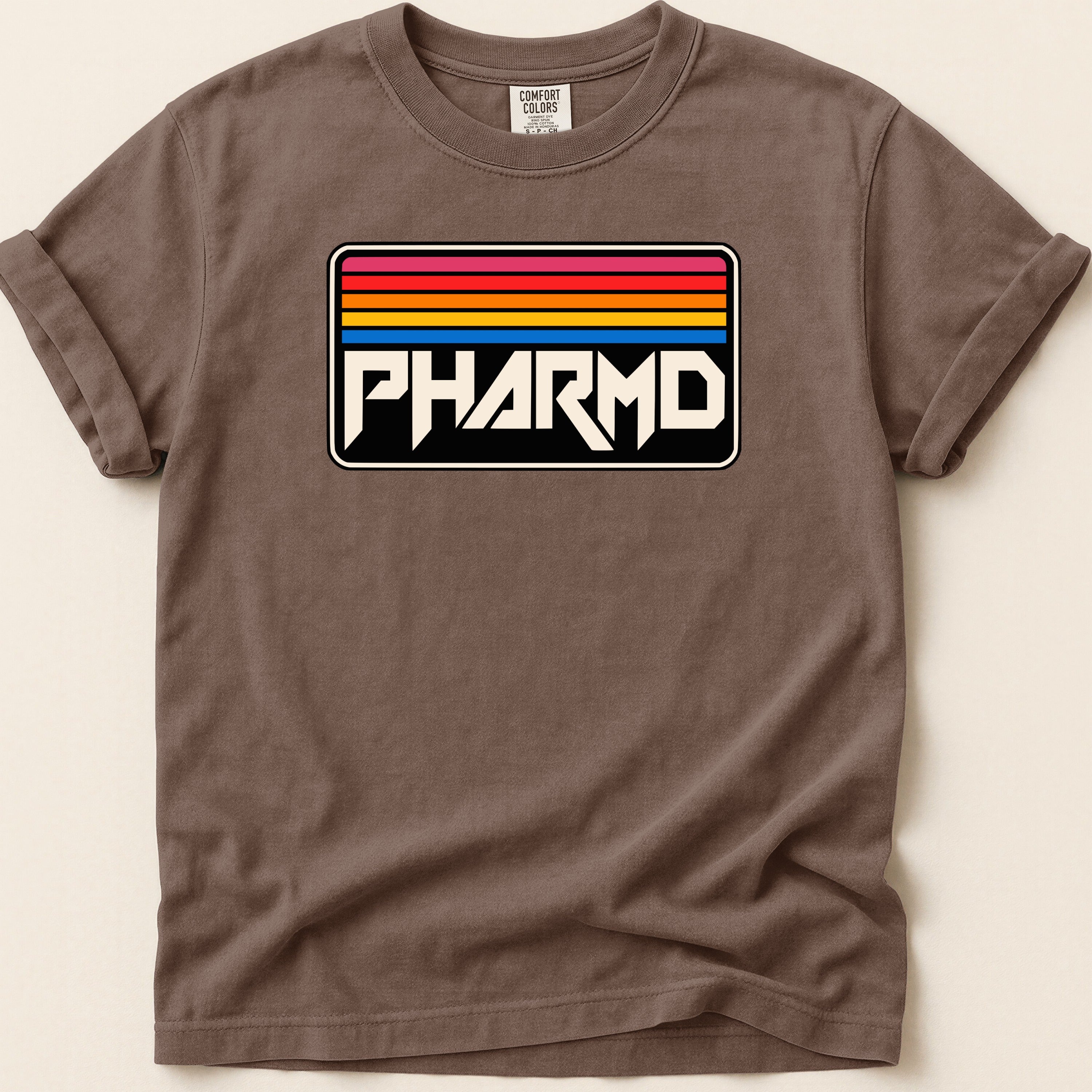 Brown t-shirt with a black rectangle displaying "PHARMD" in white amidst colorful stripes.