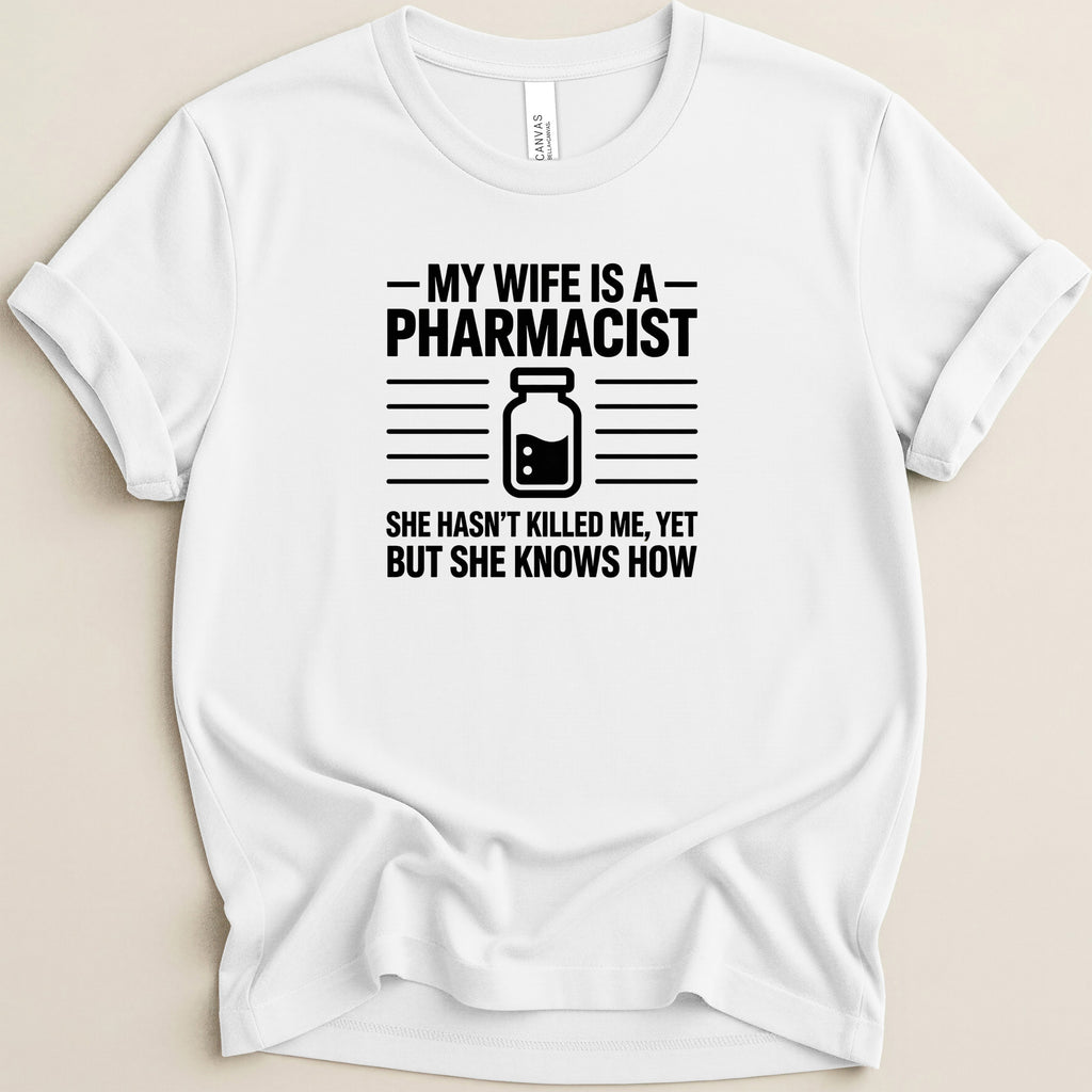 White t-shirt with "My wife is a pharmacist, she hasn't killed me, yet but she knows how" text.