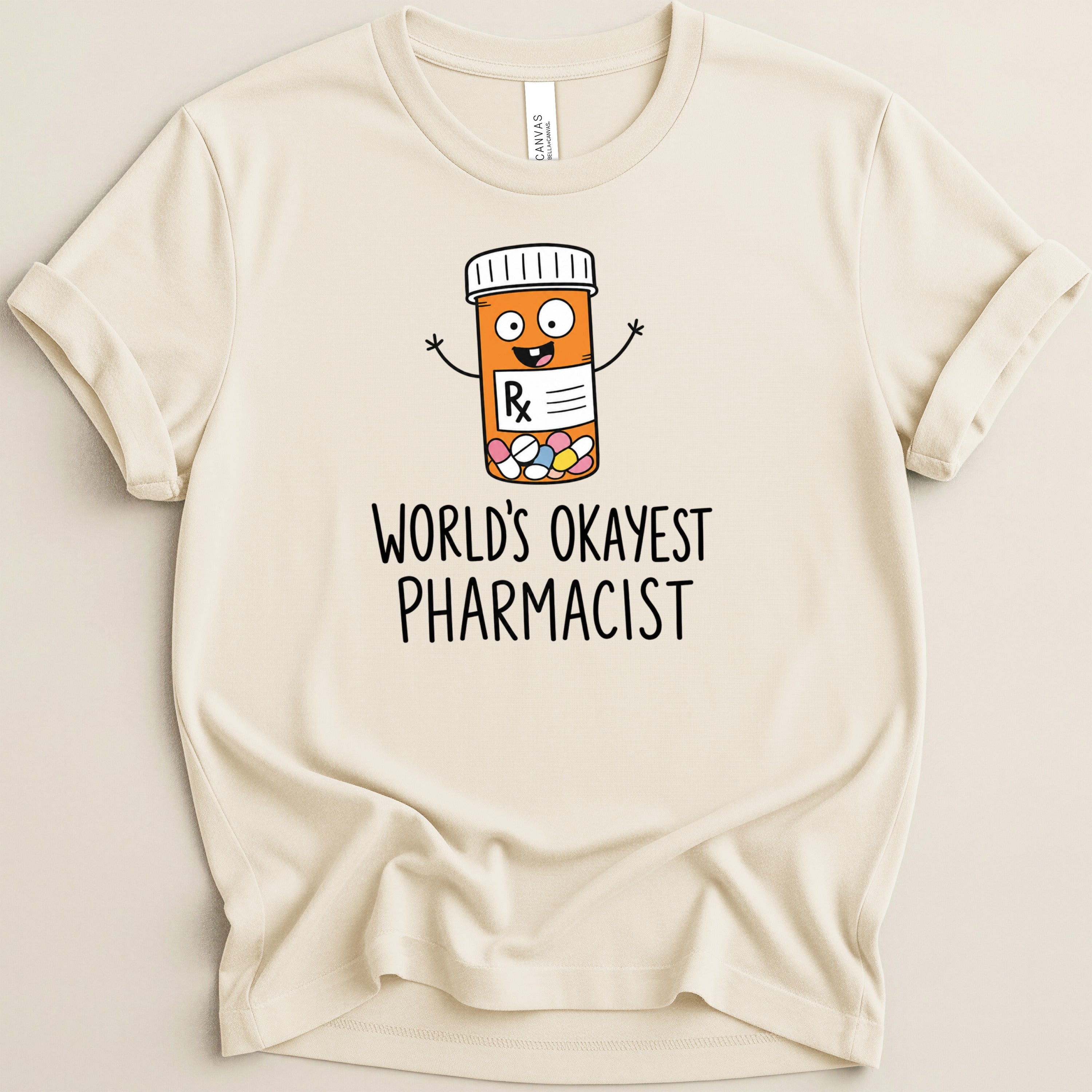 Cream t-shirt with cartoon pill bottle and "World's Okayest Pharmacist" text.