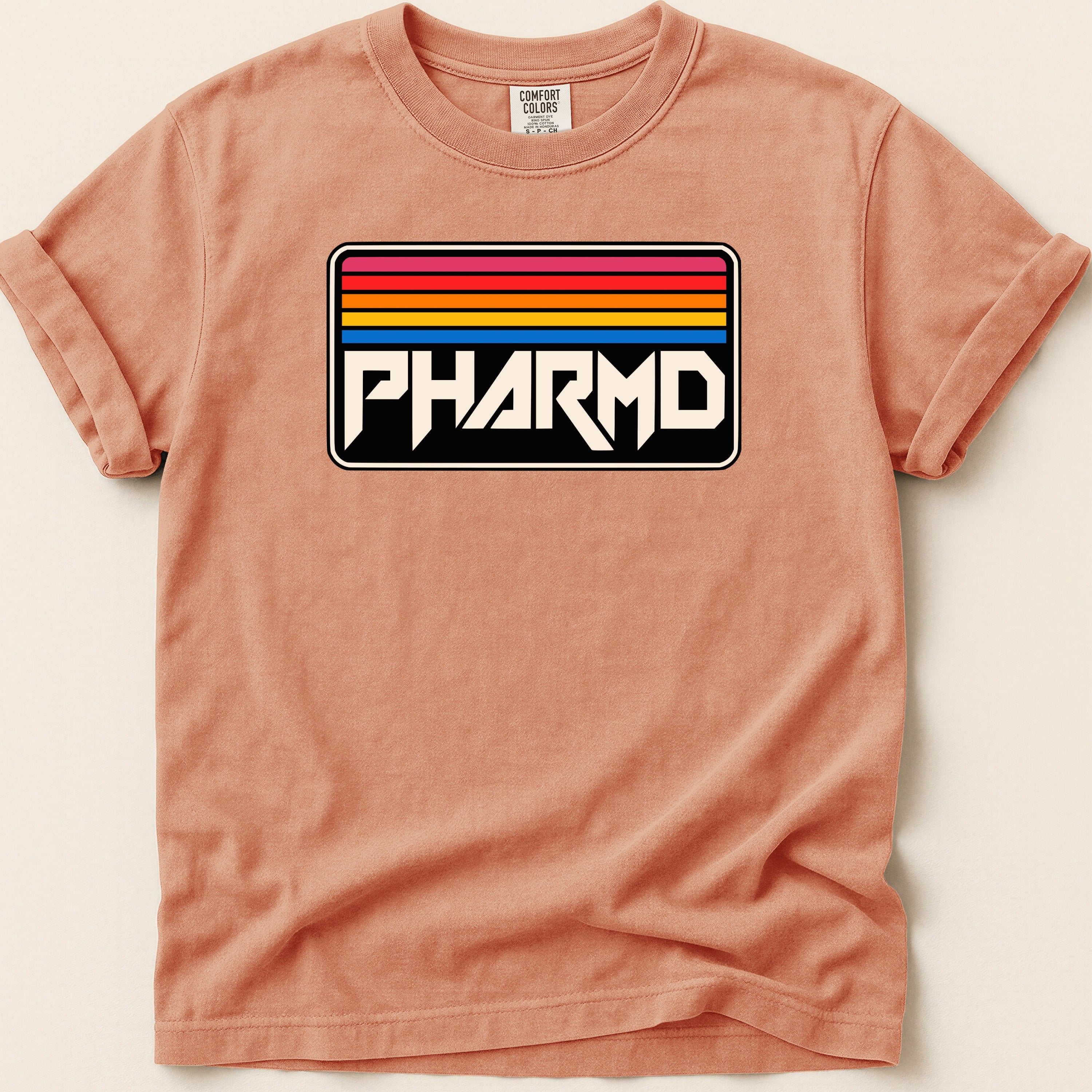 Peach t-shirt with a black rectangle logo featuring "PHARMD" and colorful stripes above.