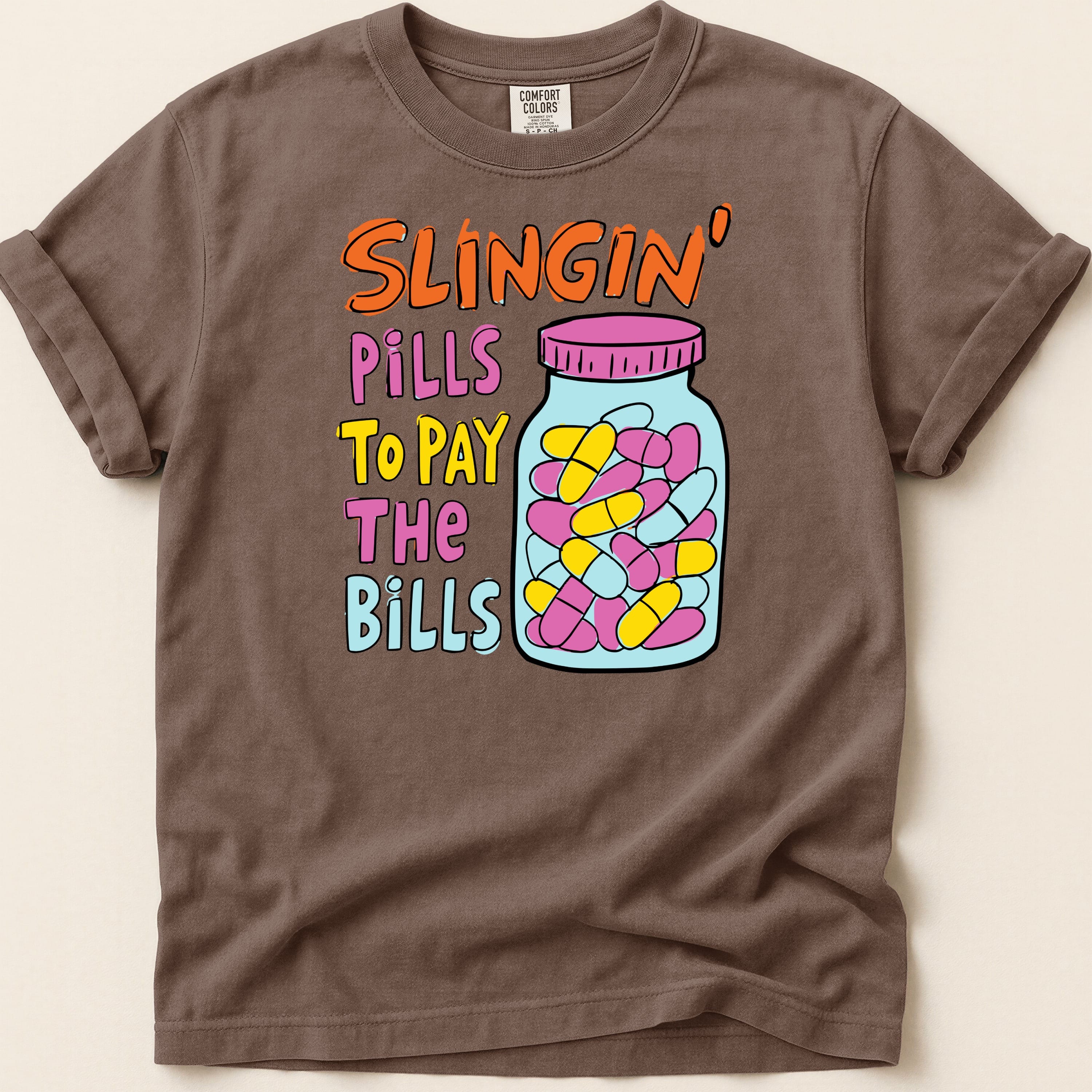 Brown t-shirt with text "Slingin' Pills To Pay The Bills" and a jar of pills.