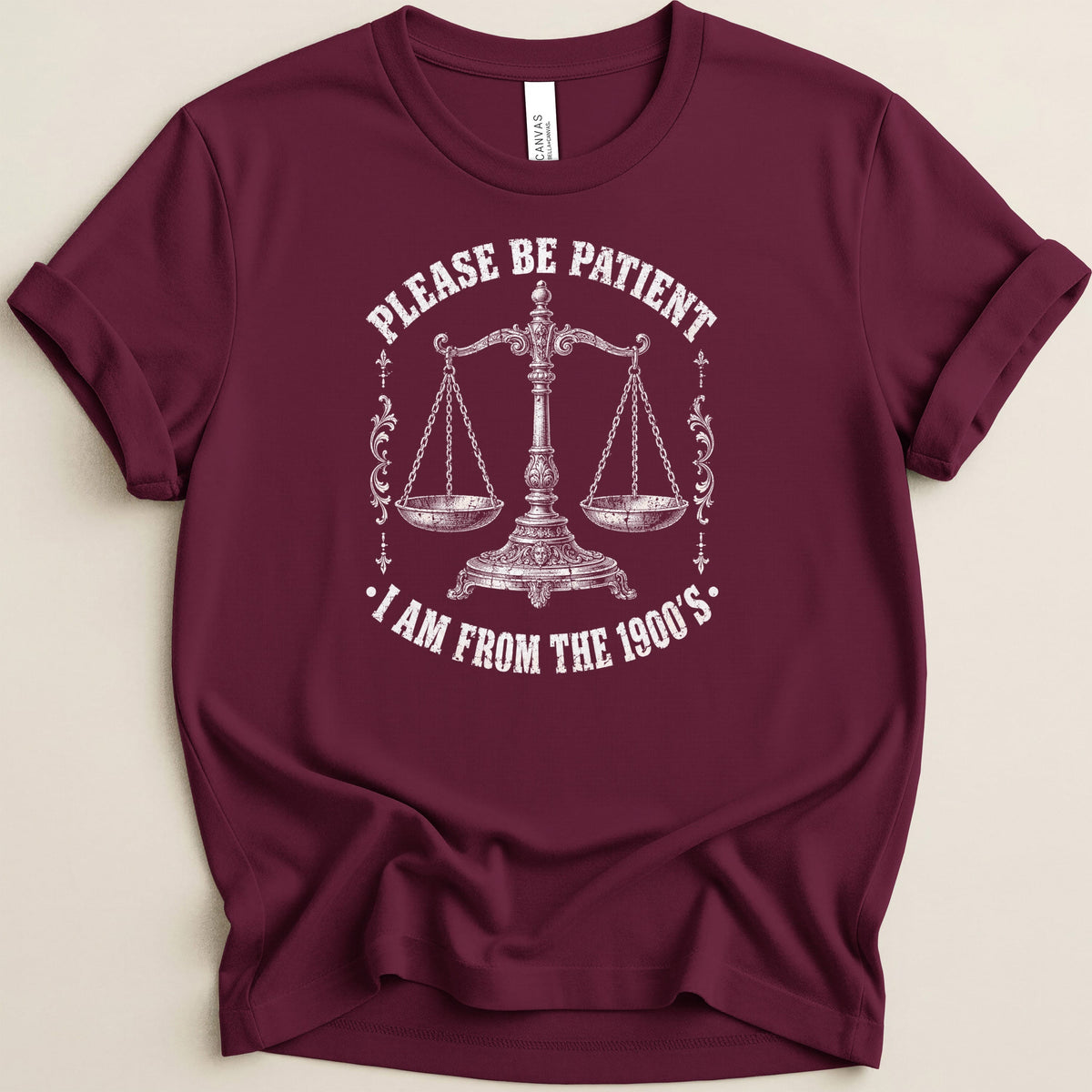 Burgundy t-shirt with white scales graphic and text: "Please Be Patient, I Am From The 1900's."