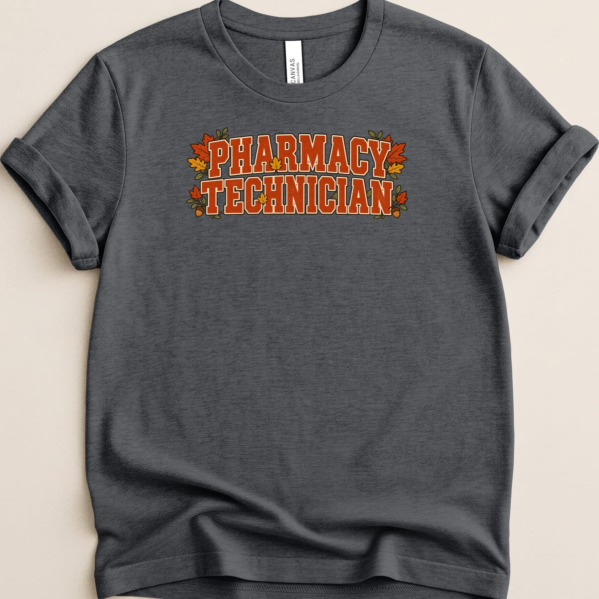 A dark gray t-shirt with rolled sleeves features orange lettering that reads "PHARMACY TECHNICIAN" decorated with fall leaves.