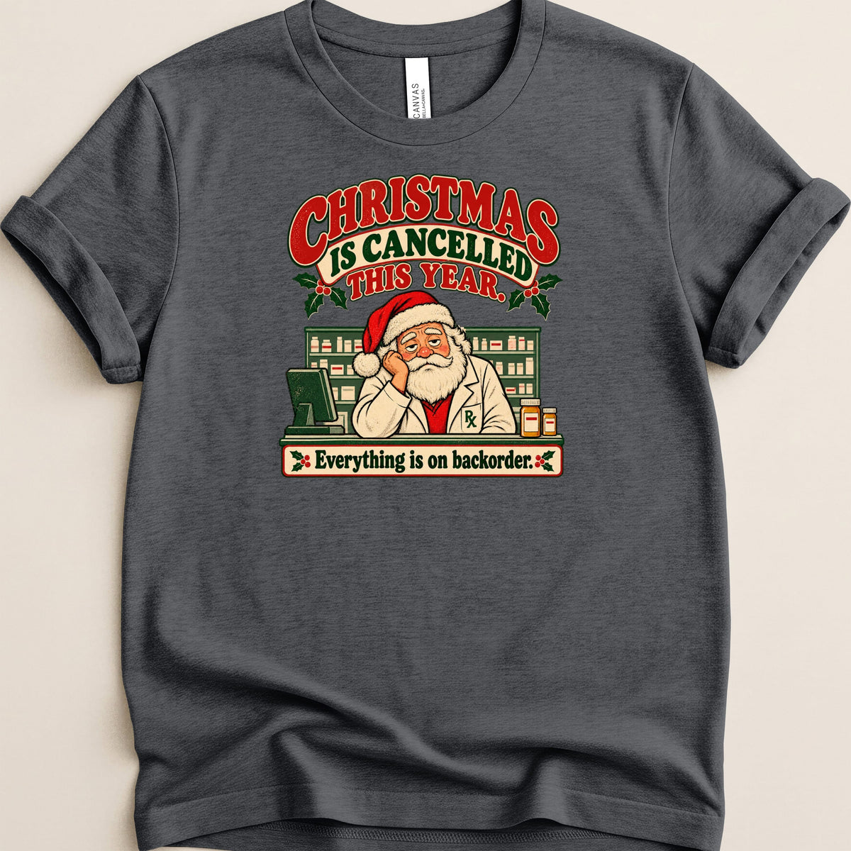 Dark grey t-shirt featuring a graphic of a tired Santa pharmacist behind a pharmacy counter with text reading Christmas is cancelled this year.