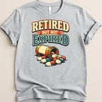 Retired but not expired text on a gray t-shirt with spilled pills.