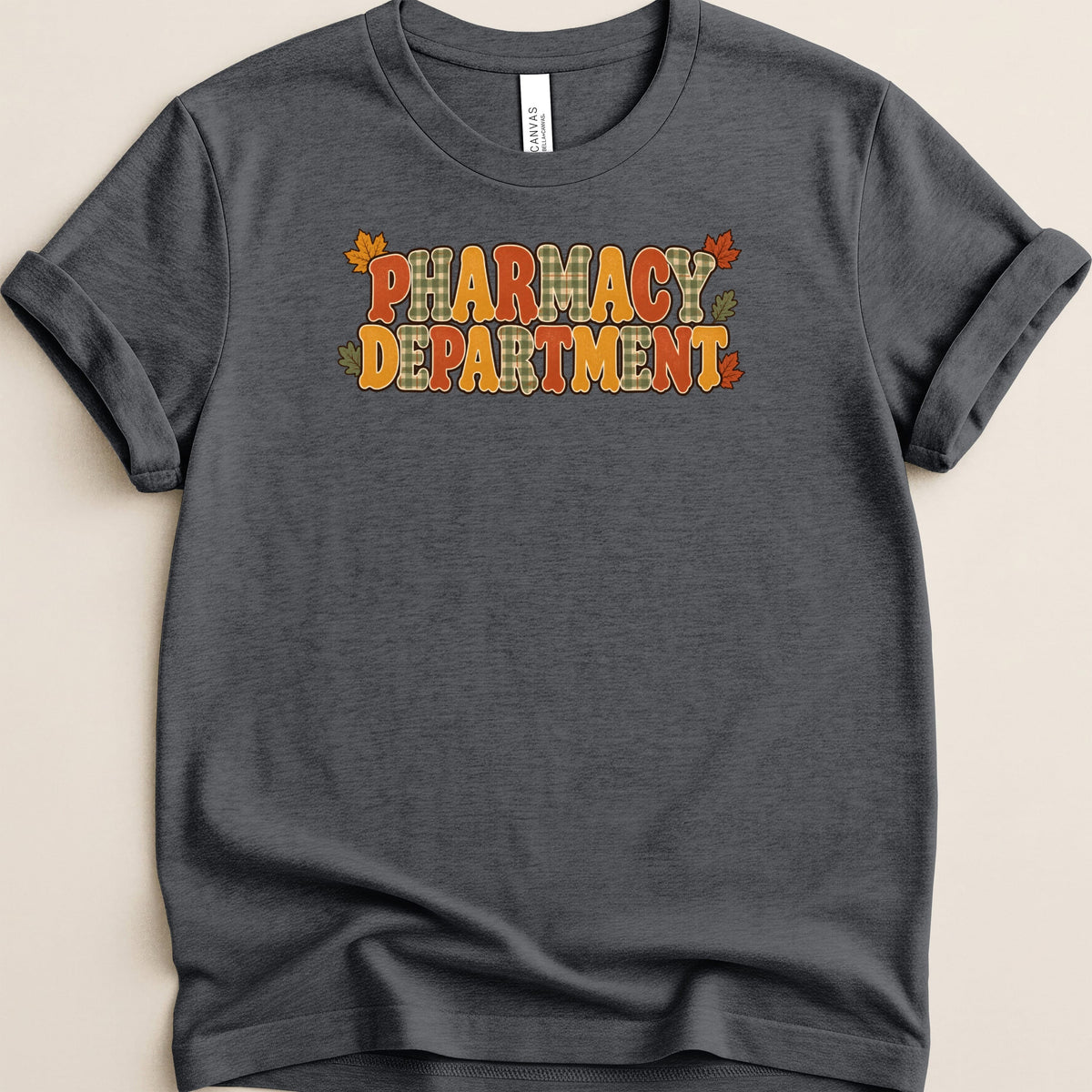 Dark grey t-shirt featuring the text "PHARMACY DEPARTMENT" in retro bubble letters with autumn plaid and leaf accents.
